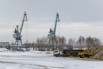 Industrial landscape in the form of two cranes of an industrial seaport and machines transporting sand.