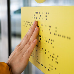 Close-up of a woman reading a braille lettering on a glass door.