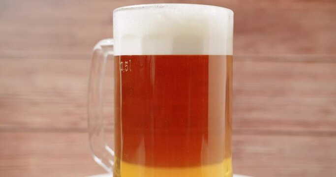 Craft Beer into the large glass. Beer Mug. On a wooden background. Half a liter, close up. Rotation 360 degrees. Glass full of beer ready to drink. 