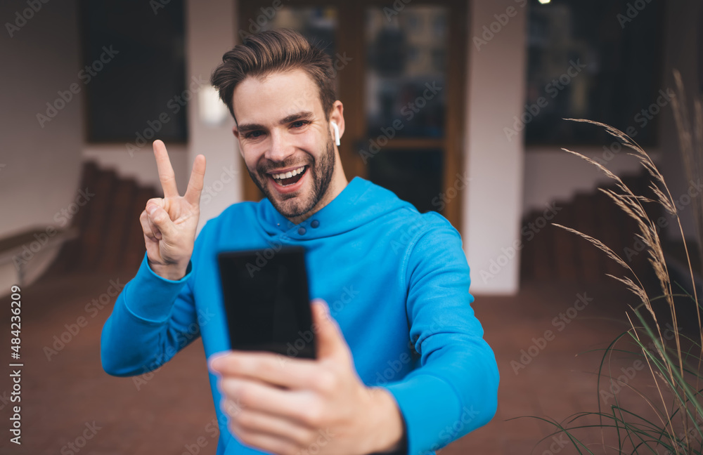 Poster joyful caucasian blogger in electronic headphones shooting live stream during web networking on smar