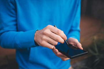 Cropped view of male blogger creating web content while networking social media via mobile phone, unrecognizable man with electronic stylus using cellular gadget for making online booking and banking