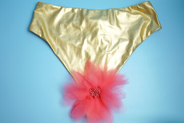 Gold-colored underpants, artificial flower. Blue background.