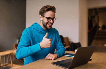 Happy male blogger have influence live stream for communicate with network followers using laptop computer and front web camera in coworking, smiling man in spectacles and earbuds make video calling