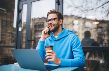 Cheerful IT professional with laptop technology making smartphone conversation for discussing web...