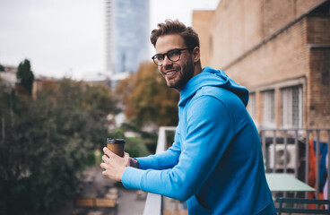 Half length of happy male model in spectacles holding disposable takeaway cup of caffeine beverage...