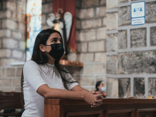 latina girl praying in the pew of an old church new reality for coronavirus pandemic selective focus