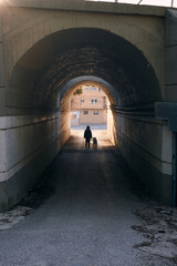 Silhouette of a woman and her dog walking through a city tunnel