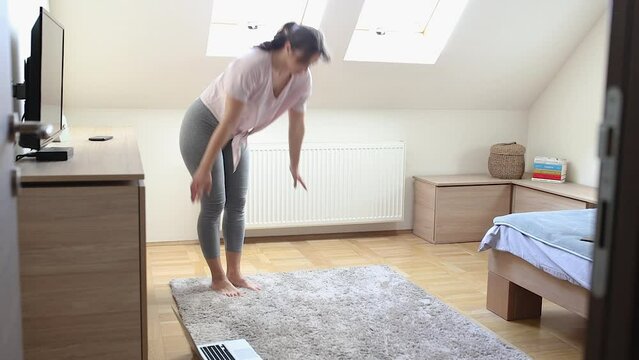 Mid-age woman doing yoga and morning exercise in her bedroom.Watching a tutorial online.