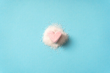 Heart-shaped marshmallows on white sugar on a blue background. The concept of diabetes and unhealthy eating. Top view.