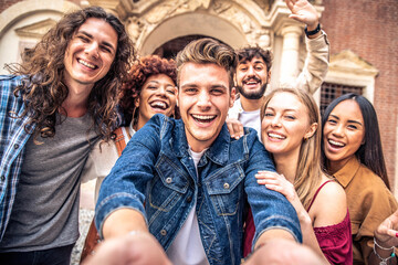 Fototapeta na wymiar Multicultural best friends having fun taking group selfie portrait outside - Smiling guys and girls celebrating party day hanging out together on city street - Happy lifestyle and friendship concept 