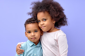 portrait of two curly adorable siblings brother and sister hugging each other, isolated on purple studio background. portrait of black birl and boy in casual wear posing looking at camera - Powered by Adobe