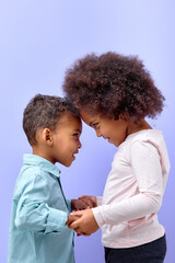 two lovely kid friends hugging holding hands together isolated over purple pastel color background, adorable kid boy and girl in casual wear posing happily. portrait. children