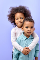 nice kind cheerful friends or brother sister friendship hugging isolated over purple color studio background. portrait of black children in casual outfit posing at camera together. copy space