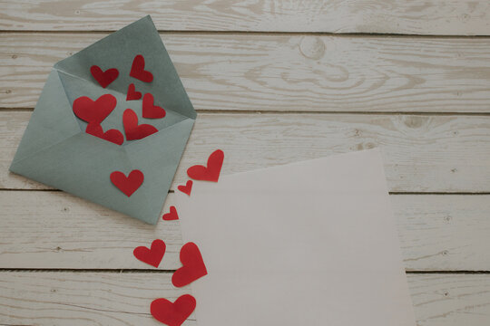 An open envelope with red hearts and a blank sheet of paper lies on a wooden background.