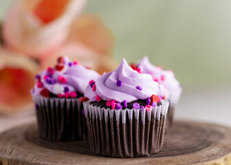 Three chocolate valentine's day cupcakes on a wooden slab and tulips blurred in the background.  Light green background.