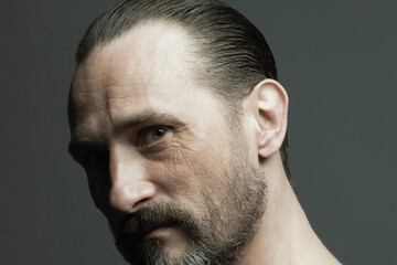 Male beauty concept. Fabulous at any age. Portrait of 45-year-old man standing over dark gray background. Hair brushed back. Rocker, biker style. Scar on forehead. Close up. Studio headshot