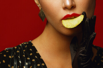 Unhealthy eating. Junk food obsession concept. Portrait of fashionable luxurious young woman holding, eating fried potato chips, posing over red background. Close up. Studio shot