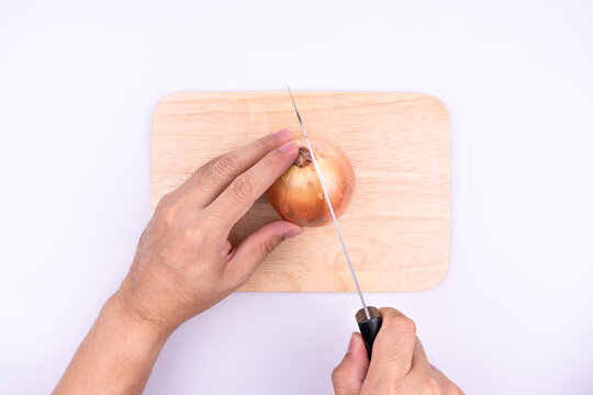Asian chef's hand is cutting onion with knife on chopping board.