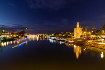Fototapeta na wymiar Sunset over the river Guadalquivir in downtown Seville with amazing colors in the sky and a view on the riverside of the Triana neighbourhood and the illuminated golder tower