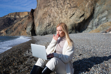 young beautiful woman talking by video link sitting on the seashore