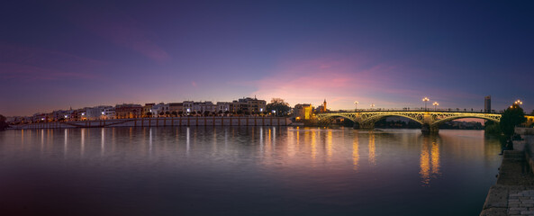 Sunset over the river Guadalquivir in downtown Seville with amazing colors in the sky and a view on the riverside of  the Triana neighbourhood.