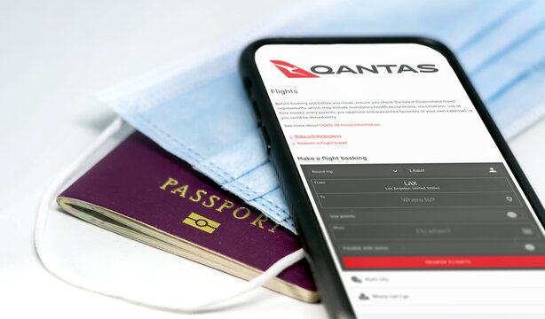 Sydney, Australia, July 2021: phone with the Qantas australian airlines app on the screen lying over a protective mask and a passport. Travel safety and restrictions during coronavirus pandemic