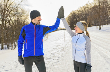 mature couple in the winter running together in nature giving an high five with there hand