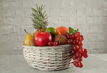 Wicker basket with different ripe fruits on grey table