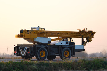 Fototapeta premium Heavy duty mobile lifting crane driving on intercity road at sunset