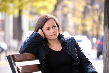 Lonely thoughtful young woman sitting alone on street bench outdoors. Solitude and depression...