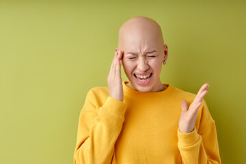 Bald annoyed caucasian lady touching head with fingers, suffering from headache. isolated on green...