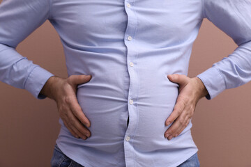 Man wearing tight shirt on pale pink background, closeup. Overweight problem