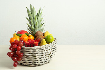 Wicker basket with different fresh fruits on white wooden table. Space for text