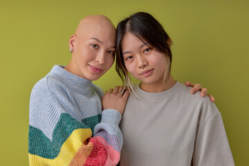 Diverse women posing at camera supporting each other, asian and another caucasian bald models,...