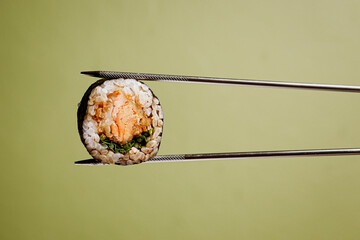 Japanese cuisine. Sushi roll in chopsticks on a green plaine  background. Foodie concept with copy space
