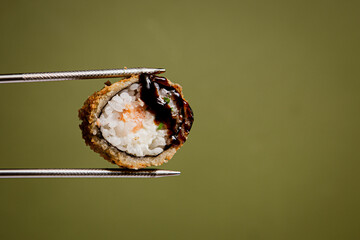 Japanese cuisine. Sushi roll in chopsticks on a green plaine  background. Foodie concept with copy space