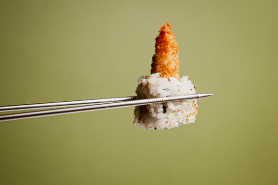 Japanese cuisine. Sushi roll in chopsticks on a green plaine  background. Foodie concept with copy space