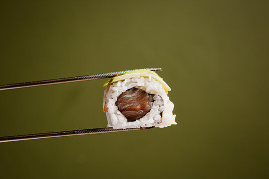 Japanese cuisine. Sushi roll in chopsticks on a green plaine  background. Foodie concept with copy space
