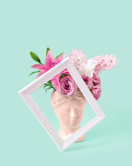 Collage with plaster antique sculpture of human face in a popart style. Creative concept colorful neon ancient statue head, hair made of fresh flowers and frame. Cyber poster on pastel mint background