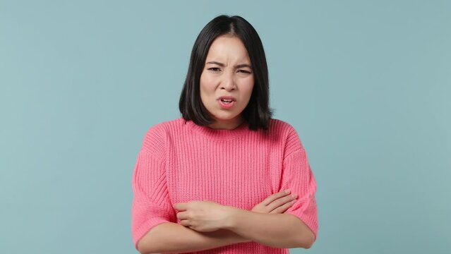 Displeased irritated sad angry young woman of Asian ethnicity 20s wears pink shirt closed eyes cover ears do not want to listen scream isolated on plain pastel light blue background studio portrait