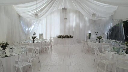 Interior design of the wedding hall, ready to receive guests. Beautiful banquet hall under a marquee for a wedding reception. Tables at the wedding banquet, drone flight inside the marquee.