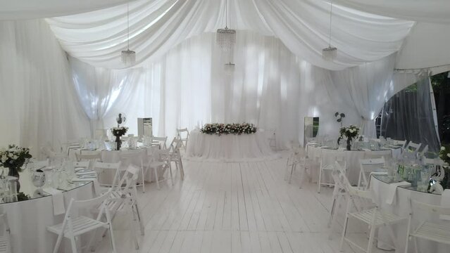 Interior design of the wedding hall, ready to receive guests. Beautiful banquet hall under a marquee for a wedding reception. Tables at the wedding banquet, drone flight inside the marquee.