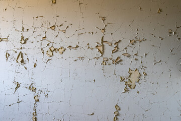 White paint on a wall peeling off. Abstract background of a vintage wall inside in an abandoned building. Interior design texture of a ruin. Backdrop of a weathered material surface.