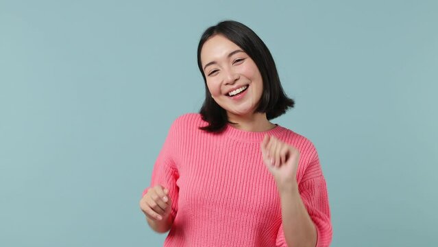Happy young woman of Asian ethnicity 20s wear pink shirt dance waving rising expressive gesticulating hands fooling around have fun enjoy isolated on plain pastel light blue background studio portrait