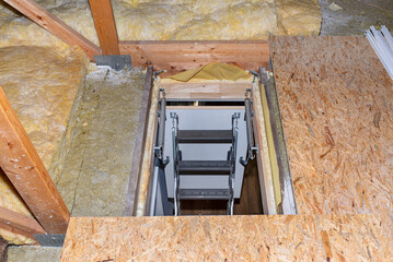 Sliding metal stairs to the attic in the ceiling, open flap and unfolded stairs, modern look. View...