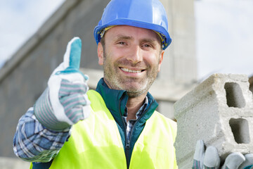 man showing thumb-up builds a brick wall