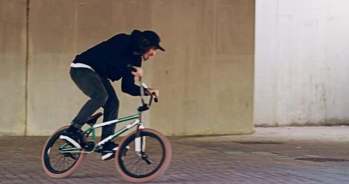 Young bmx biker doing tricks on his bike under a bridge. Young male biker having fun doing tricks with his bike outside.