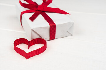 Valentine's Day or birthday concept with copy space. Red ribbon heart and gift box on white wood