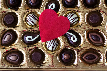 Assorted chocolates in a box and a red decorative heart. Valentine's day concept.