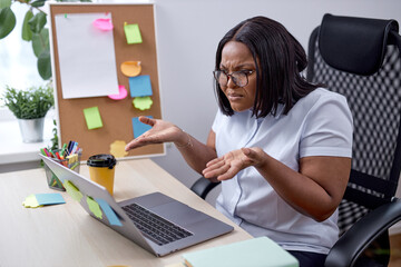 angry frustrated black woman spreading arms misunderstanding, working online on laptop in modern...